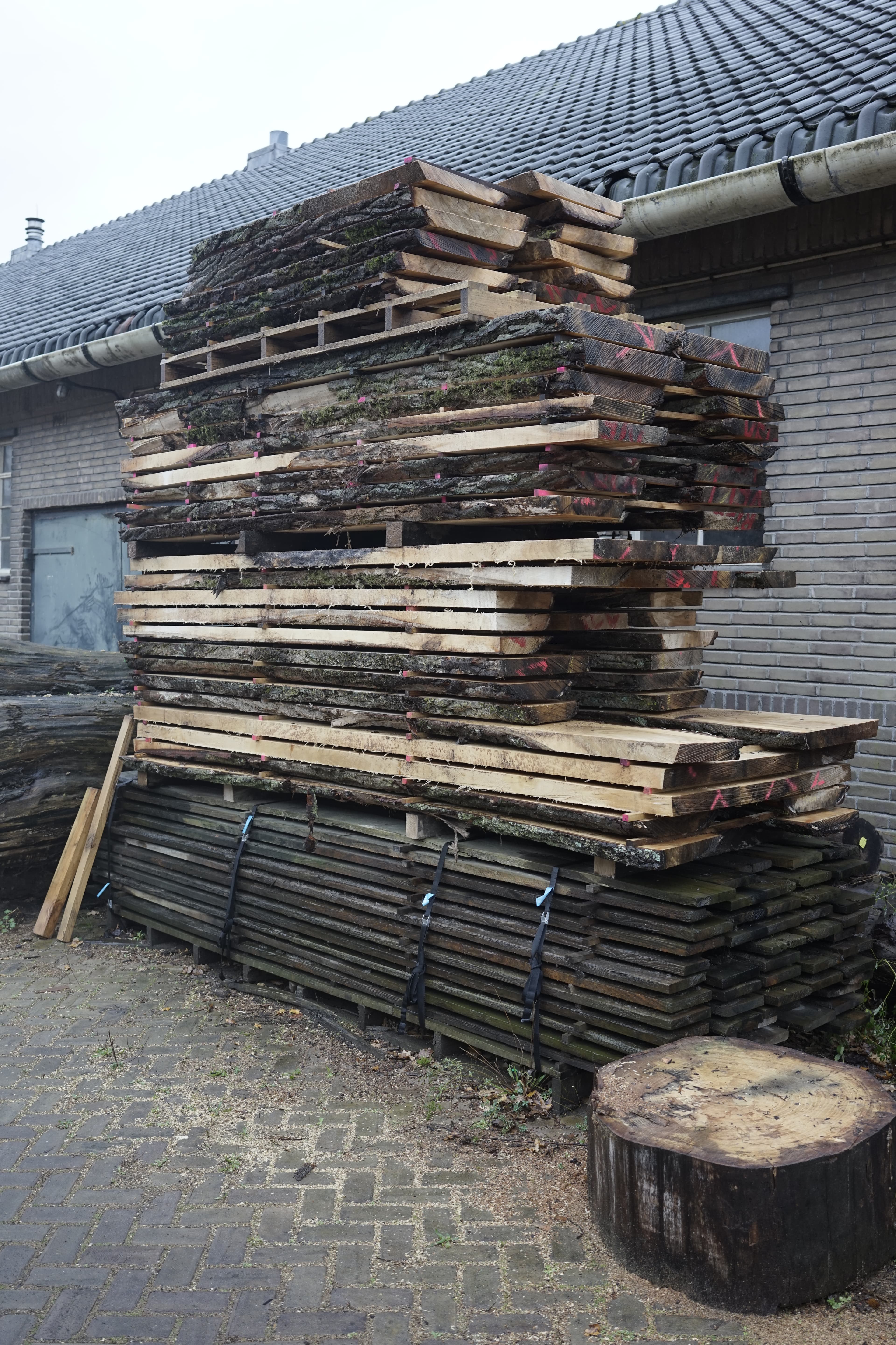 A stack of poplar planks standing on the open air next to a workshop building to dry. 